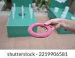 Small photo of Hand holding a red rubber ring for throwing rings in throwing rings where players can throw green and blue rings into a white stick. Players help each other to throw as many rubber rings down the pole