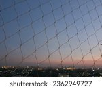 See through through plastic netting or nylon netting. (Used to prevent items from falling for elite residents or not to allow birds to nest.) During sunset, dark skies and bokeh created by street ligh