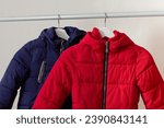 Red and blue child down jackets hanging over white background