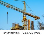 Small photo of Yellow construction tower crane. High-altitude slewing crane on a background of blue sky and tree crowns