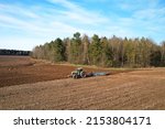 Small photo of Tractor with plow on soil cultivating. Green tractor plowing field, drone view. Cultivated land and soil tillage. Agricultural tractor on field cultivation. Tractor disk harrow on plowing farm field.