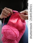 Small photo of Woman knitting a wool knit pink scarf with knitting heedless, portrait style