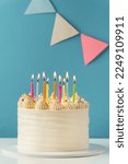 Small photo of Birthday cake with white cream cheese frosting decorated with multicolored lit candles on a blue background. Happy Birthday concept. Tradition of making a wish while blowing out candles on a cake