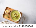 Bowl of broccoli cream soup with parmesan cheese, crunchy croutons and microgreen on a wooden tray, top view. Spring vegan recipe, healthy food, detox, menu. Copy space for text