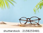 Trendy glasses in plastic frame on beach with palm leaves. Glasses sale poster. Optic store sale-out offer. Copy space. Optic store discount. Eyewear fasion promotion. Eyeglass Tortoiseshell frame