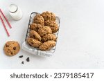 Homemade low-calories banana cookies with oatmeal, dark chocolate drops and walnuts in a metallic basket and a bottle of milk on light background. Copy space. Healthy food. Oatmeat biscuits.