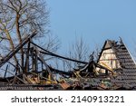 Small photo of Conflagration concept, Damaged and broken roof top of the house, Destroyed house from fire with blue sky and trees as background, Burned wooden roof and bricks tile.