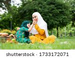 Small photo of Happy Asian family Arabic Muslim mother and little girl child with hijab dress smiling, talking, learning apportion and having fun moment good time in park. Happy Muslim family mom and child concept.