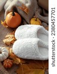 Small photo of Slippers and autumn leaves and pumpkin. White soft slippers in an autumn composition. Warm weekend in home aesthetics. Warm soft winter slippers.