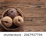 Small photo of Knitting needles and yarn of beige and brown in a wicker basket on a wooden background. View from above. Handicraft day concept. Place for text.
