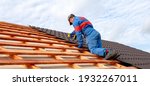 Small photo of Man worker uses a power drill to attach a cap metal roofing job with screws.