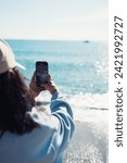 Small photo of a young girl takes a selfie on her phone on the seashore. happy girl calling via video chat on the seashore. A blogger girl takes a selfie on the seashore. sea holiday.