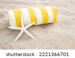 Small photo of Rolled up striped white and yellow towel, white starfish shell on the sandy beach. Sunny day. The concept of tanning, vacation, relaxation, retreat, vacation, travel, sunbathing. Copy space.