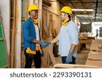 African American and Caucasian carpenter man shake hands together with smiling after success in wood work project in factory workplace.