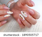 Delicate white and pink manicure with gold design. Shiny gold design. Female fingers with long nails and pink gel polish with sequins.