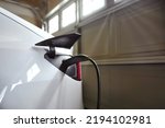 Small photo of White EV electric car plugged with battery charger and charging in garage at home. At home charing station brings more convenient, less expensive and more cost savings comparing to supercharger.
