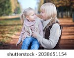 Small photo of Scene of quiet family happiness filiation and love. Happy caucasian mother holding her little daughter on her laps face to face closely looking into each others eyes in park in warm sunny autumn day.