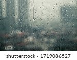Small photo of Closeup raindrops water droplets trickling down on wet clear window glass during heavy rain against blurred city view in rainy day monsoon season