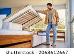 Small photo of A man chooses a bed in a store, examines a frame with slats. Purchase of a mattress, bed and other sleeping accessories.