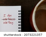 Coffee cup notebook with handwritten text I AM WORTHLESS, changed to I AM WORTHY, concept of positive self talk affirmation to overcome negative thoughts from low self esteem, accept one own value