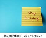 Small photo of Yellow note stick on blue copy space background with handwritten text STOP BULLYING, concept of stop hurting or frightening someone else by degrade or demean victims just to feel powerful or stronger