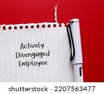 Small photo of Pen and torn paper on red background with handwritten text Actively Disengaged Employee - means employees who are unhappy at work and busy undermining workplace by getting other to share discontent