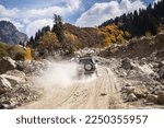 White SUV car climbs a dusty road in the autumn mountains.