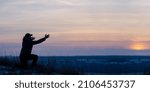 Small photo of Prayer. Repentance. Silhouetted men on a background of blue sky and sunset. Kneeling Prayer to God. Glorification. Praising God