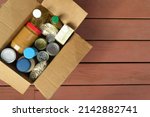 Small photo of A box of donated canned goods and non-perishable foods for a food pantry for the poor sitting on red, wood panel background. Copy space.