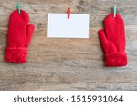 Small photo of Knitted red mittens and blank page one horizontal line are fastened with clothespins to the ropes on a wooden background. Winter, Valentine Day concept.