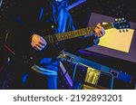 Small photo of Closeup of young latino guitarist and keyboardist with hoodie and black guitar playing live in a concert under yellow and blue lights in the night