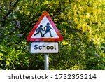 Small photo of school sign in London, UK. Warning to slow down road sign with trees in the background