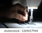 Small photo of Hand is inserting thread into pin hole of white industrial sewing machine closeup.