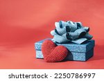 Knitted heart Blue sparkling gift box with ribbon bow on red background. Gift or holiday concept. Mothers Day, Fathers birthday wedding or St Valentines day with copy space. Minimal banner