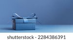 Small photo of small Luxury gift box with a blue bow on dark blue table. Side view monochrome . Fathers day or Valentines day gift for him. Corporate gift concept or birthday party. Festive sale copy space banner