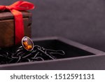 Small photo of Cinnamon stone ring in brown box on black background and wooden box with red ribbon. Stone ring concept