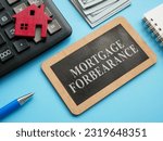 Small photo of Wooden plate with inscription mortgage forbearance and model of house.