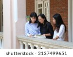 Small photo of Female professor supervisor or school teacher with glasses discuss with young university girl undergraduate postgraduate students over a book at corridor of old red-brick building in campus