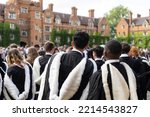 Small photo of back view of Male and female fresh graduate international British Black African students with gown and academic address walk in campus Selwyn College, Cambridge University, UK on congregation day.