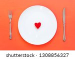 Small photo of Red heart on a white plate with cutlery on a pink background. lady-killer or heartbreaker concept. Maneater or womanizer.