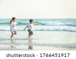 Happy Asian family little child girl and boy running and playing together on the beach at summer sunset. Smiling adorable sibling brother and sister relax and having fun in holiday vacation travel.