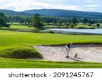 Small photo of Confidence Asian man hitting golf ball from a bunker to the green at golf course in sunny day. Healthy male golfer enjoy leisure activity outdoor sport golfing at golf country club in summer vacation