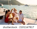 Small photo of Group of man and woman friends enjoy party drinking champagne with talking together while catamaran boat sailing at summer sunset. Male and female relax outdoor lifestyle on tropical travel vacation