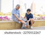 Small photo of Elderly man suffering knee pain during jogging exercise with his son at park in the city. Adult man gives first aid to father with knee injury. Family relationship and older people health care concept