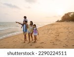 Happy Asian family travel ocean on summer holiday vacation. Parents and children kid enjoy and fun outdoor activity lifestyle walking and playing together at tropical island beach at summer sunset.