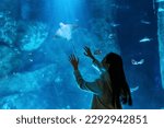 Young Asian woman looking shoal of fish in large glass tank during travel Aquarium in Japan. Attractive girl enjoy and fun learning and looking sea life at oceanarium on holiday vacation.
