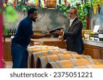 Professional African man wine shop worker explaining and recommending wine to customer at liquor store. Sommelier tasting wine in winery. Winery or brewery manufacturing industry and winemaker concept