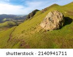 Small photo of in early morning,spring sunlight,a large bare rock sitting on a grassy steep slope of Caer Caaradoc hillside,incongruous in the foreground.