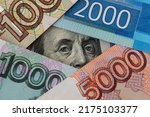 Small photo of The hundred dollar bill with Franklin's portrait surrounded by russian banknotes of various denominations. Close-up of President Franklin's eyes. Concept of ruble exchange rate.