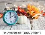 Set your clocks and fall back. Clock and decorations of mini pumpkins, colorful autumn leaves, antlers and bokeh lights over a white wooden table. Daylight saving time concept. 